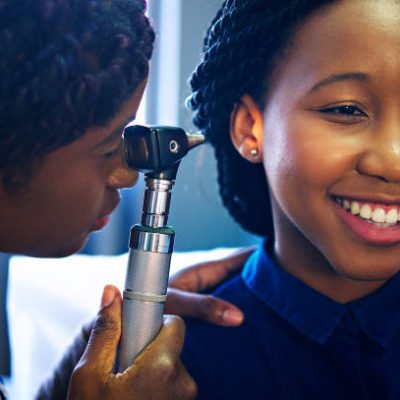 A young African-American female doctor examining a young female patient's ear with a diagnostic otoscope in a hospital ward in Cape Town South Africa